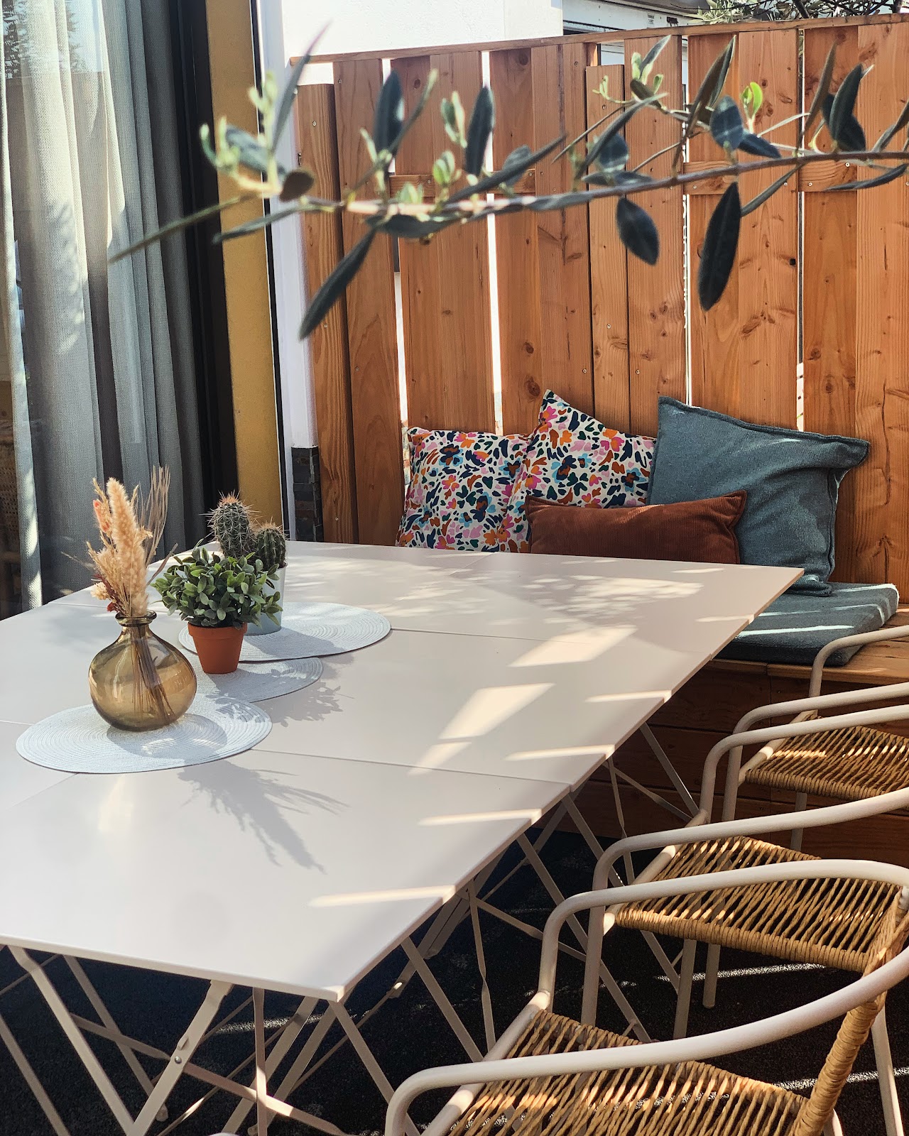 Terrasse ensoleillée avec table blanche, chaises en rotin et banquette coussins colorés