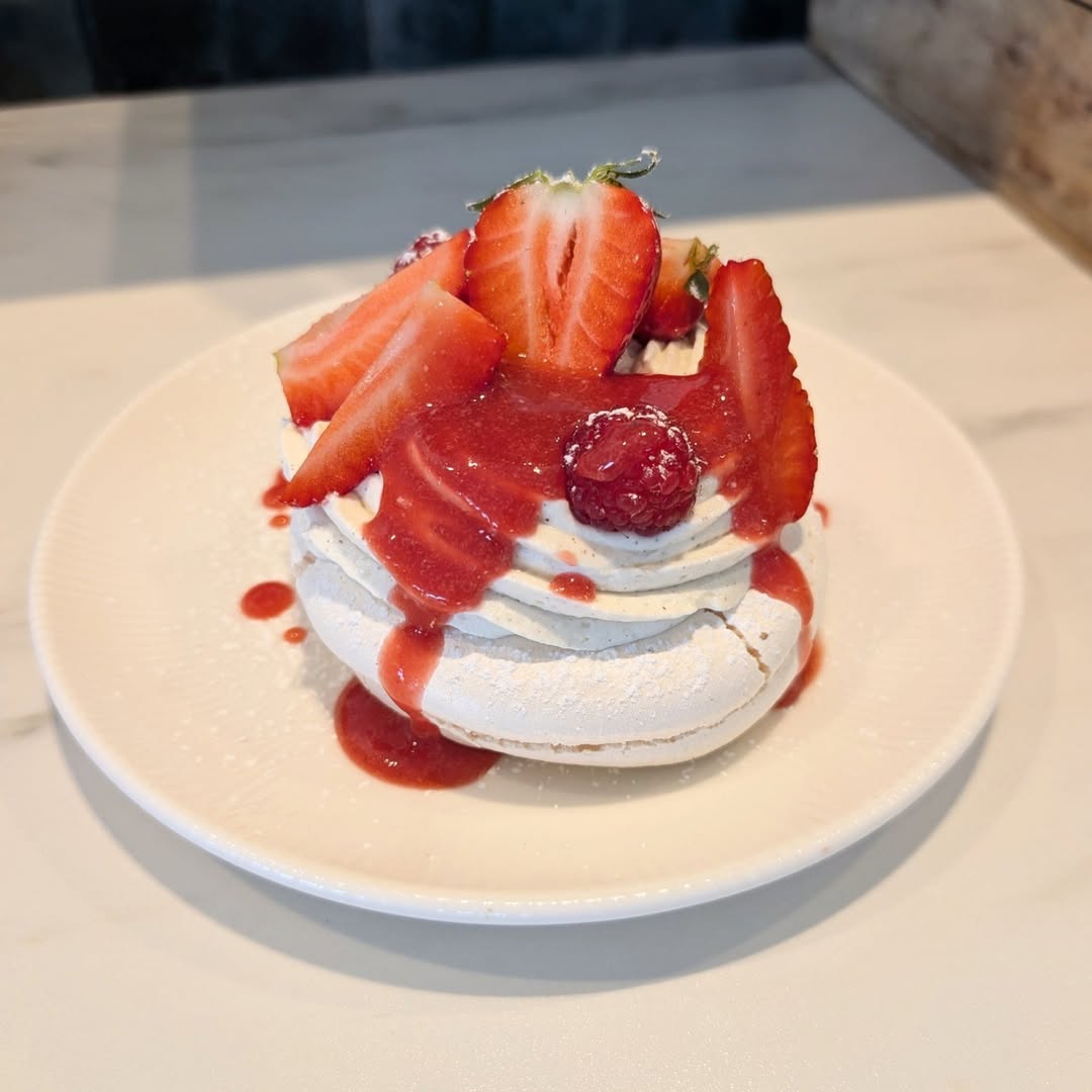 Pavlova aux fraises et framboises avec coulis rouge sur assiette blanche