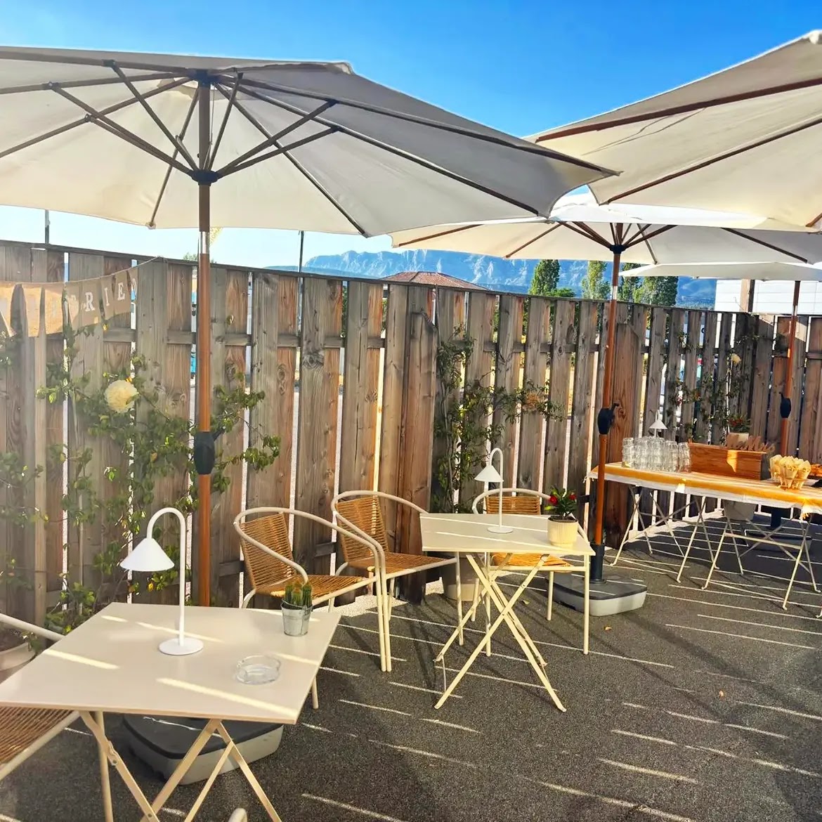 Terrasse ensoleillée avec parasols blancs, tables et chaises en rotin, vue montagne